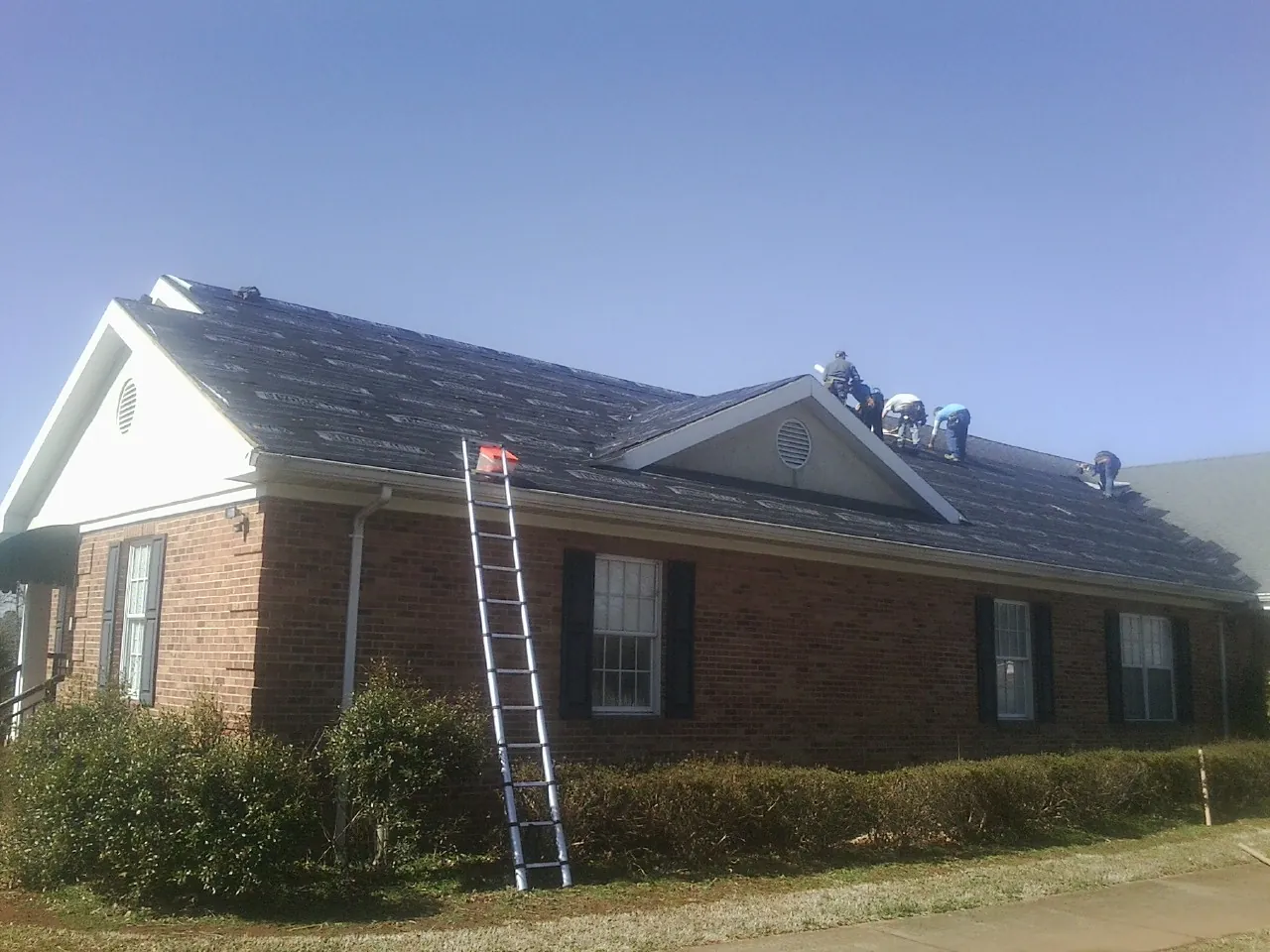 Crew tearing shingles off a brick ranch roof with a ladder set — Emergency Roof Repair work by our crew in Moorpark