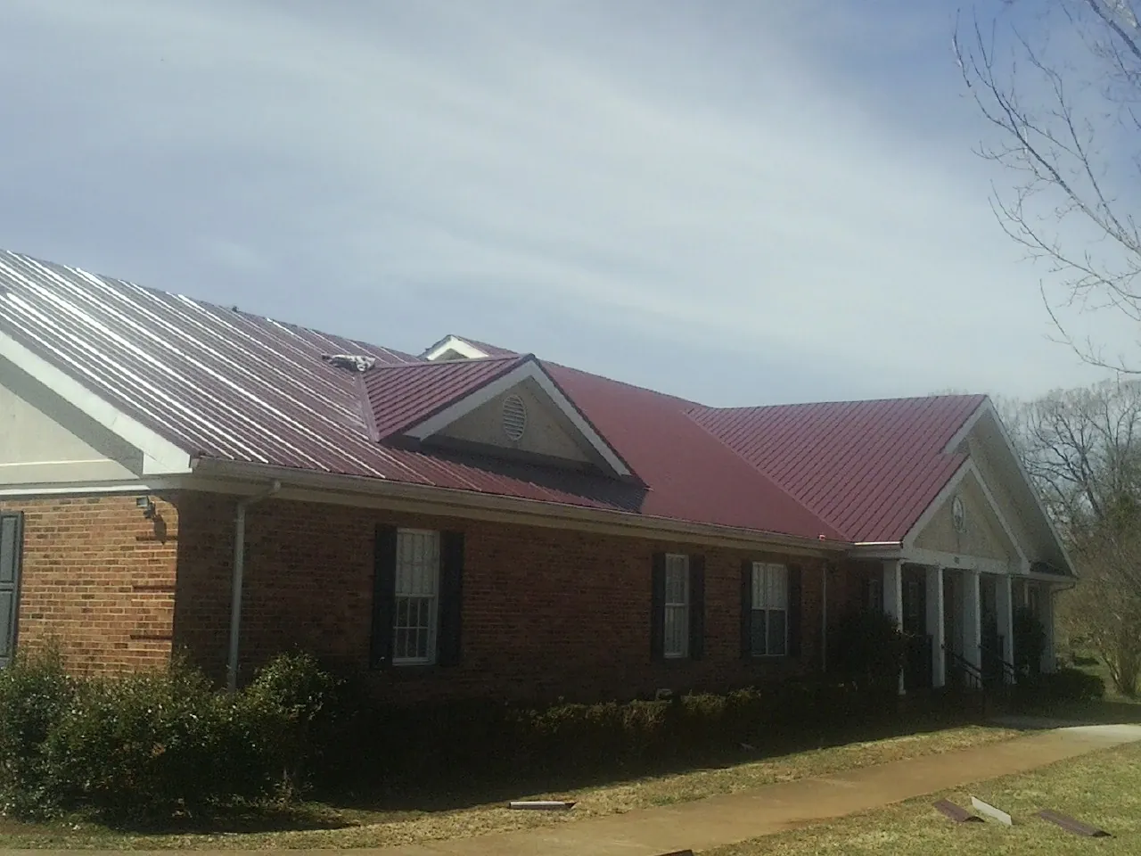 Red metal roof with gabled entries on a long brick building, from a Hail Damage Roof Repair job in Moorpark