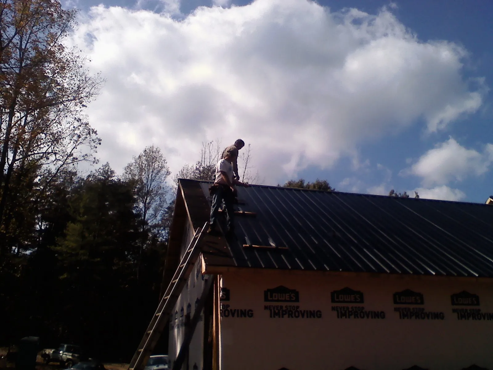 Roofer fastening dark metal panels high against a cloudy sky, from a Roof Inspection job in Moorpark
